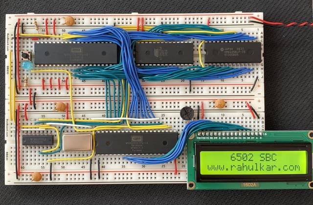 A 6502 computer built on two breadboards: a W65C02 CPU, EEPROM and RAM chips wired with blue and yellow jumpers, and a green LCD reading 6502 SBC www.rahulkar.com
