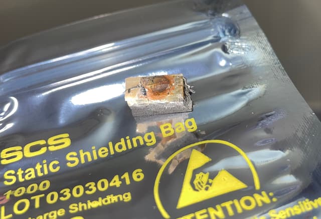 A small chip set in a broken-off block of potting compound, with fine leads at both ends, on a silver anti-static bag.